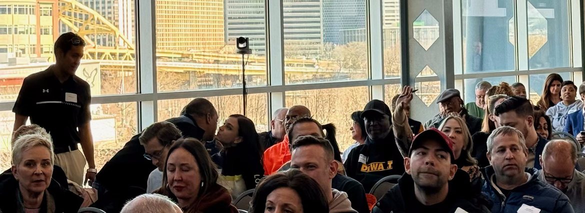Attendees at a community session with the Pittsburgh skyline through the windows behind them